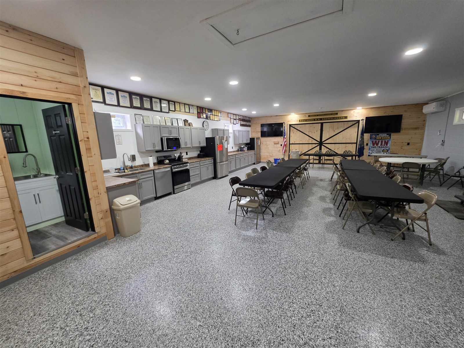 Wide view of the clubhouse with tables, speckled flooring, wood accents and barn-style doors.