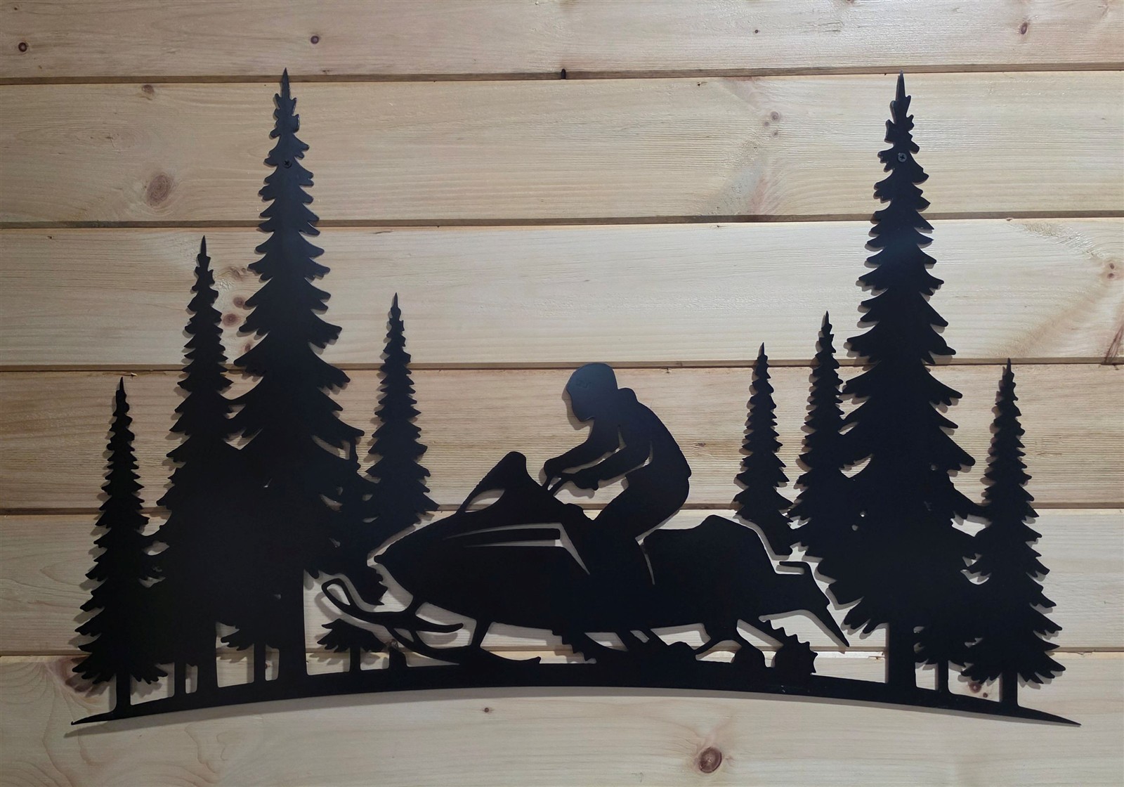 Metal snowmobile and evergreen tree artwork mounted on a wood wall.